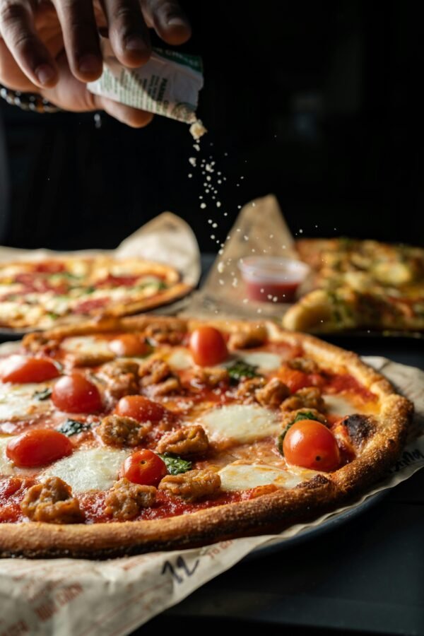 Close-up of a freshly baked pizza with cherry tomatoes, mozzarella, and herbs being sprinkled by hand.