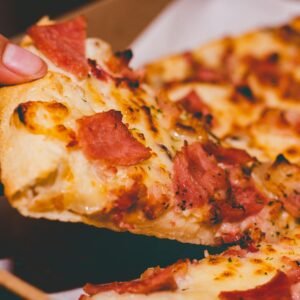 Close-up of a hand holding a delicious slice of pepperoni pizza.